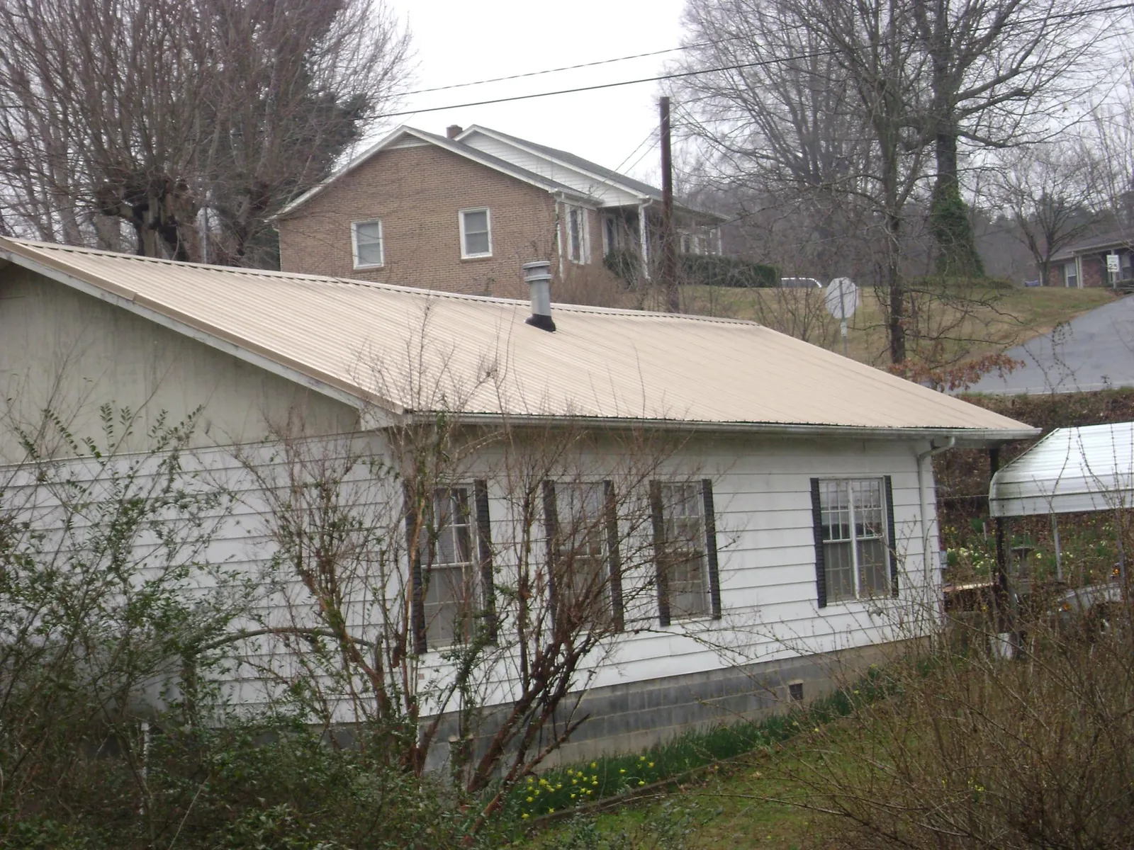 Tan metal roof on a white sided house set into a hillside — Commercial Roofing by Roofing Brothers in Springfield